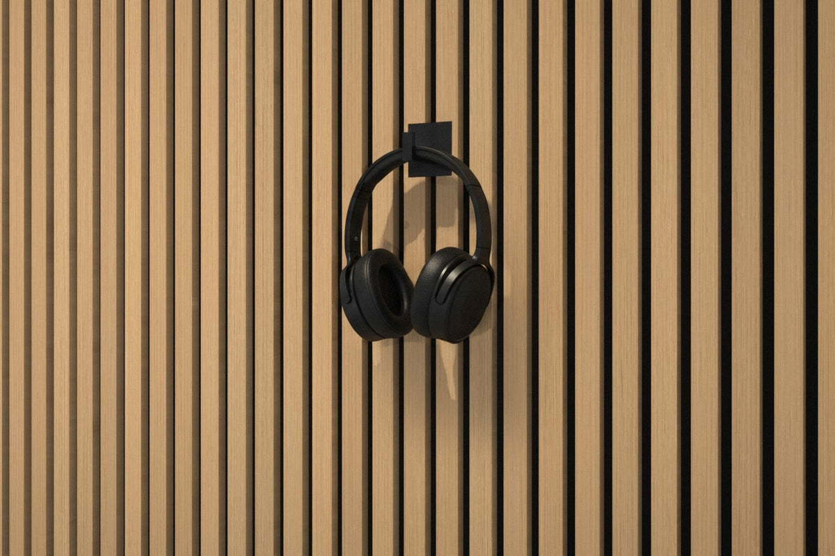 Matte-black steel wall hook on an oak slat wall holding headphones