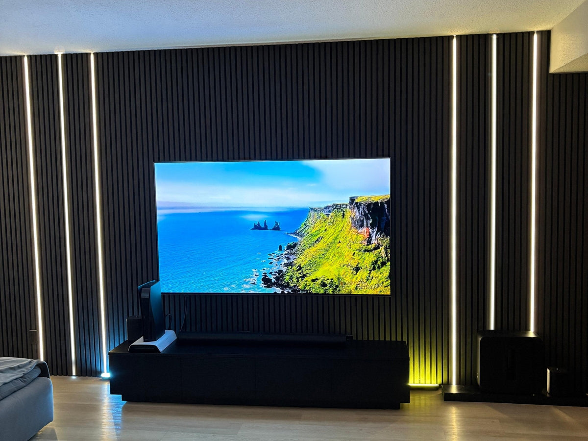 Black slat TV wall with six white LED strips set inside the felt gaps, three on each side of the TV